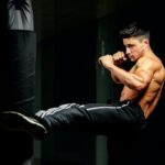 muscular handsome fighter giving a forceful forward kick during a practise round with a boxing bag